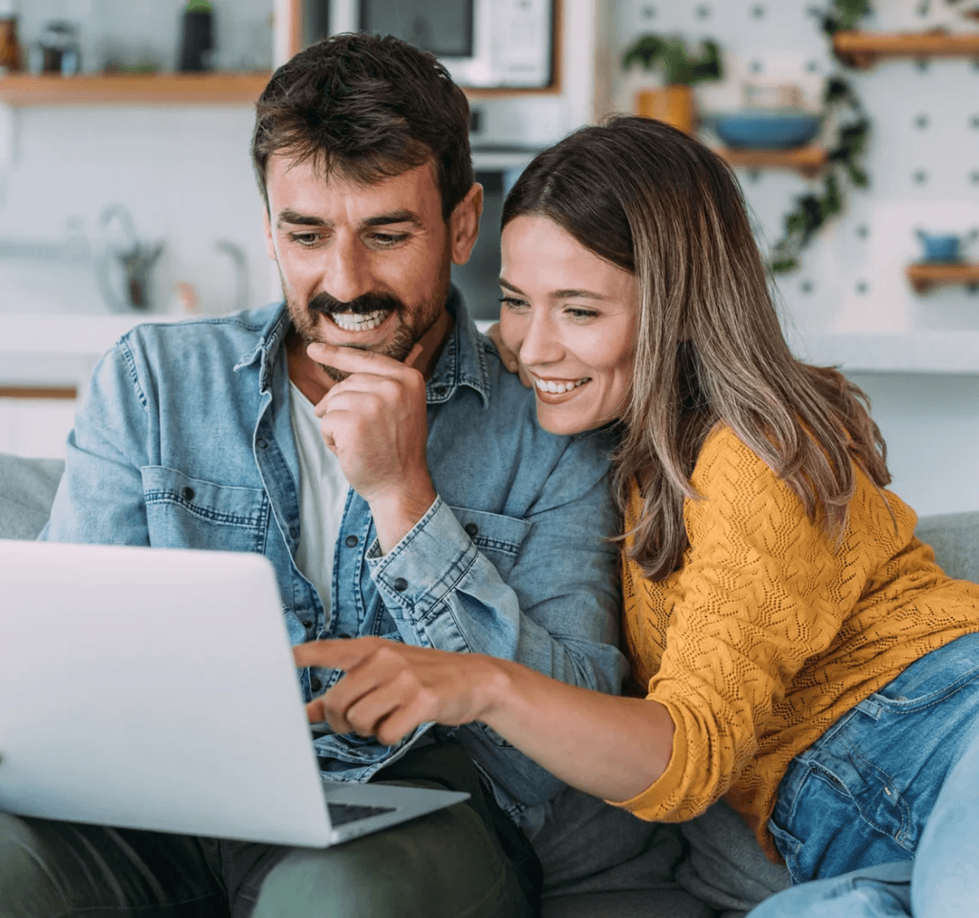 A joyful couple huddled over a laptop in their sunny kitchen, brainstorming together